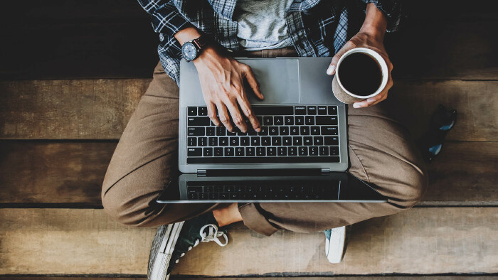 © Akira Kaelyn, stock.adobe.com Mann sitzt mit Laptop und Kaffee am Boden